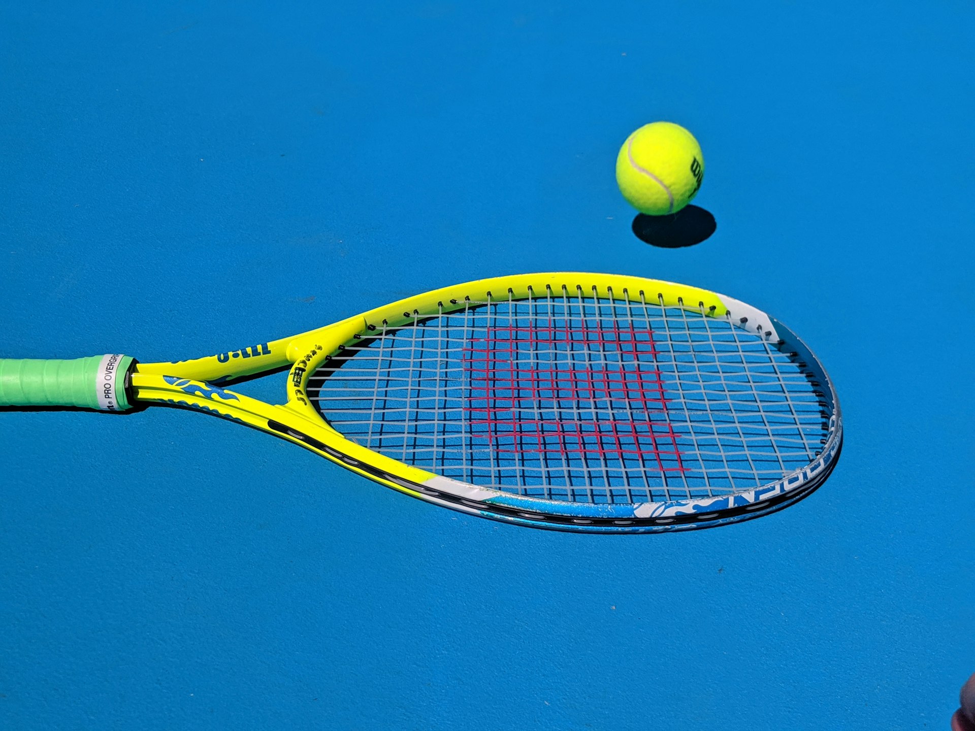 A yellow tennis racket and ball against a bright blue sky