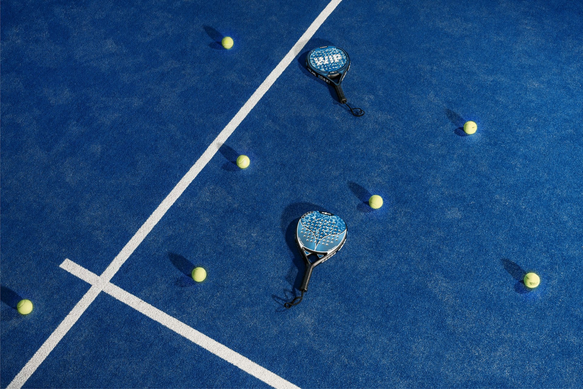 Padel rackets and balls laid out on a blue padel court