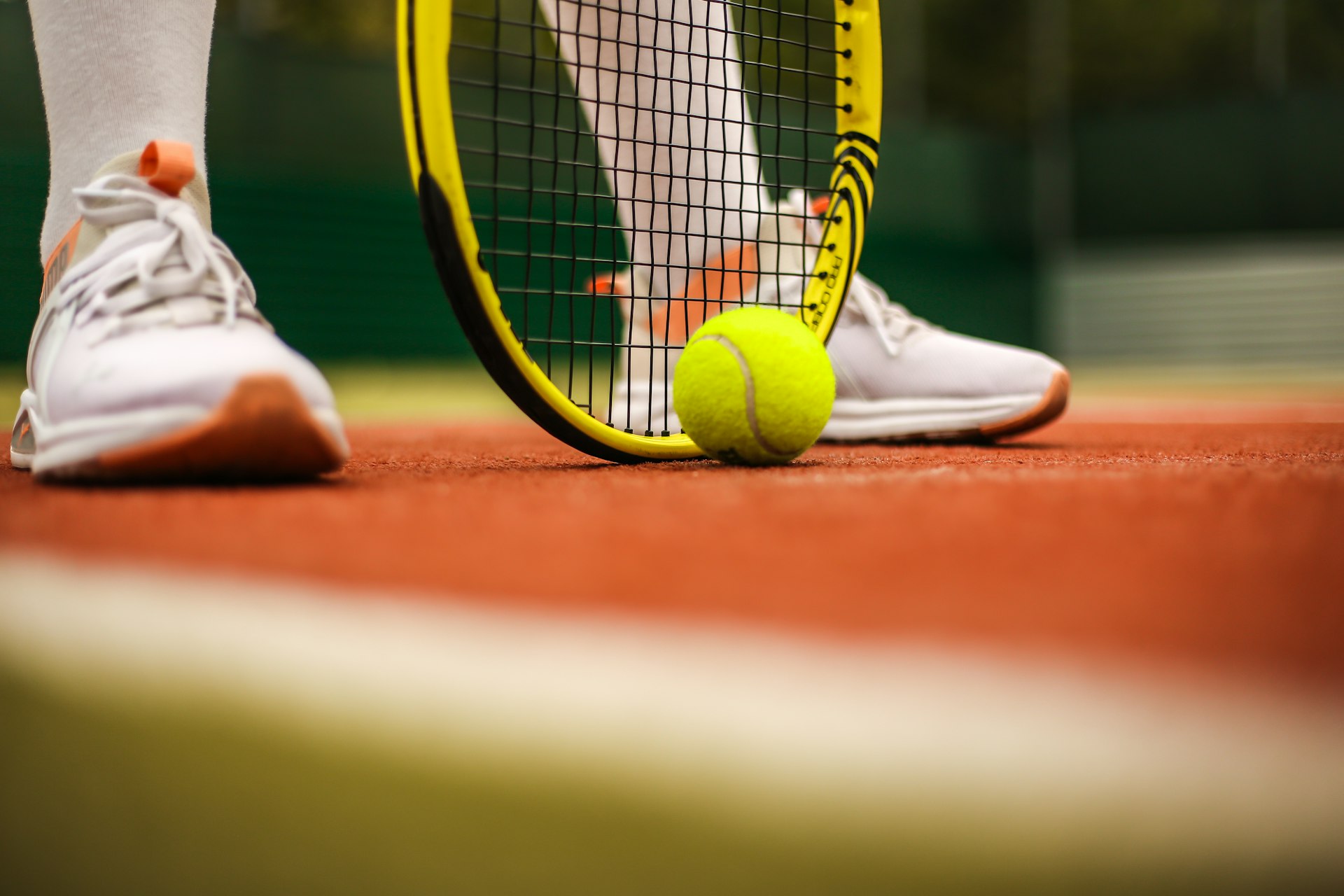 Tennis shoes, racket and ball on a clay court