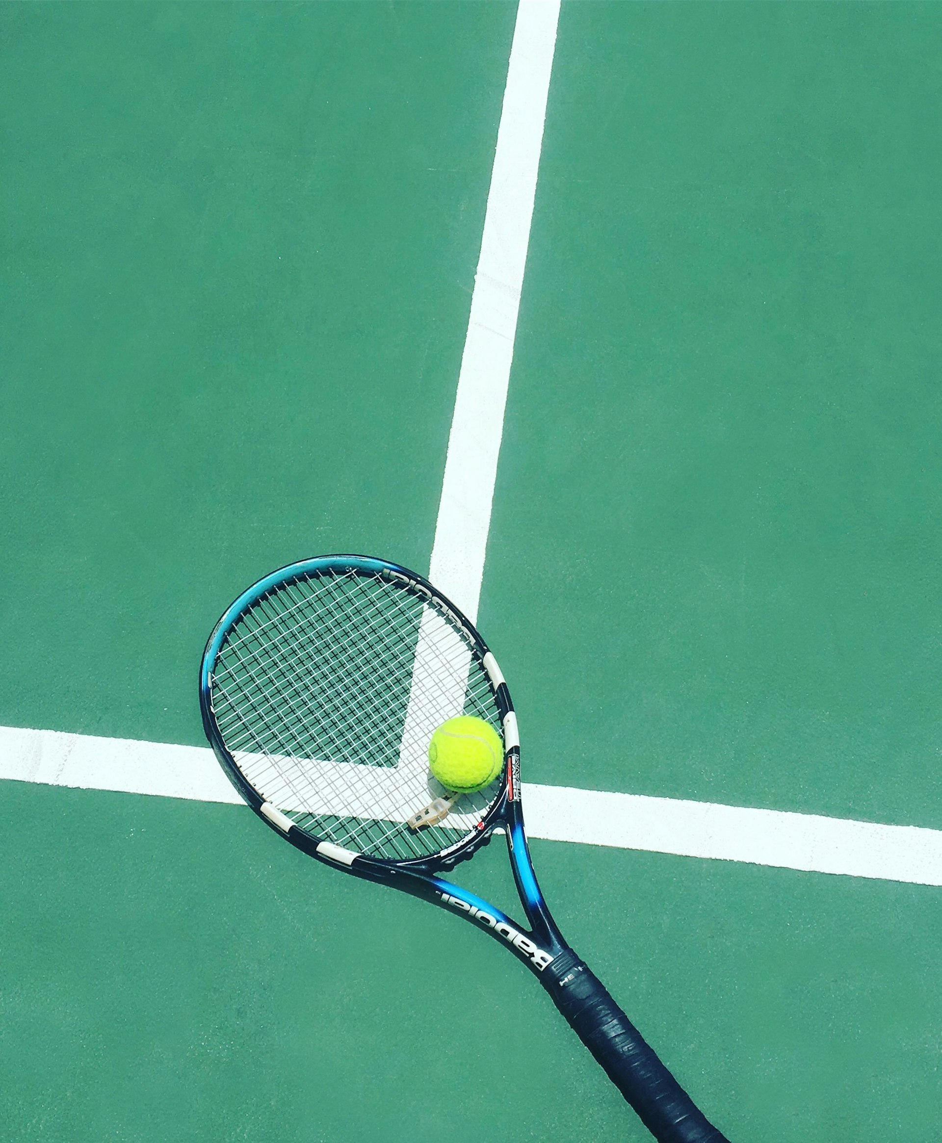 A tennis racket and ball resting on the baseline of a green court